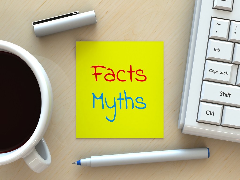 Facts and myths written on a sticker note with a laptop, coffee, and pen