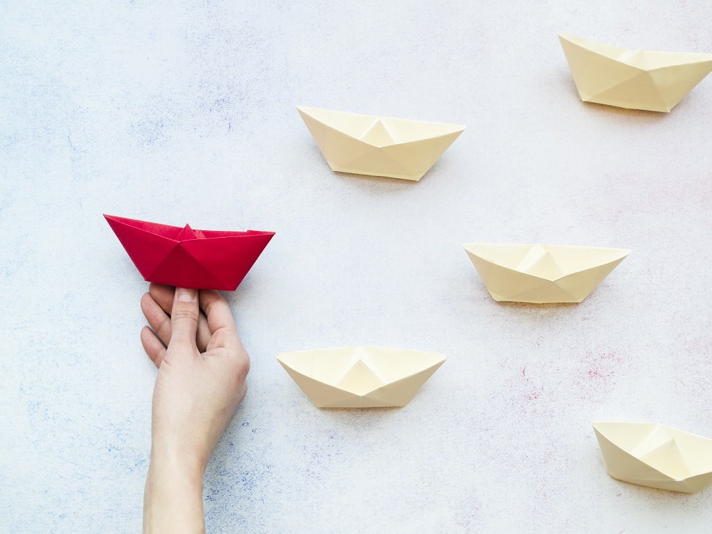 A person holding a red paper boat and five white paper boats are aside.